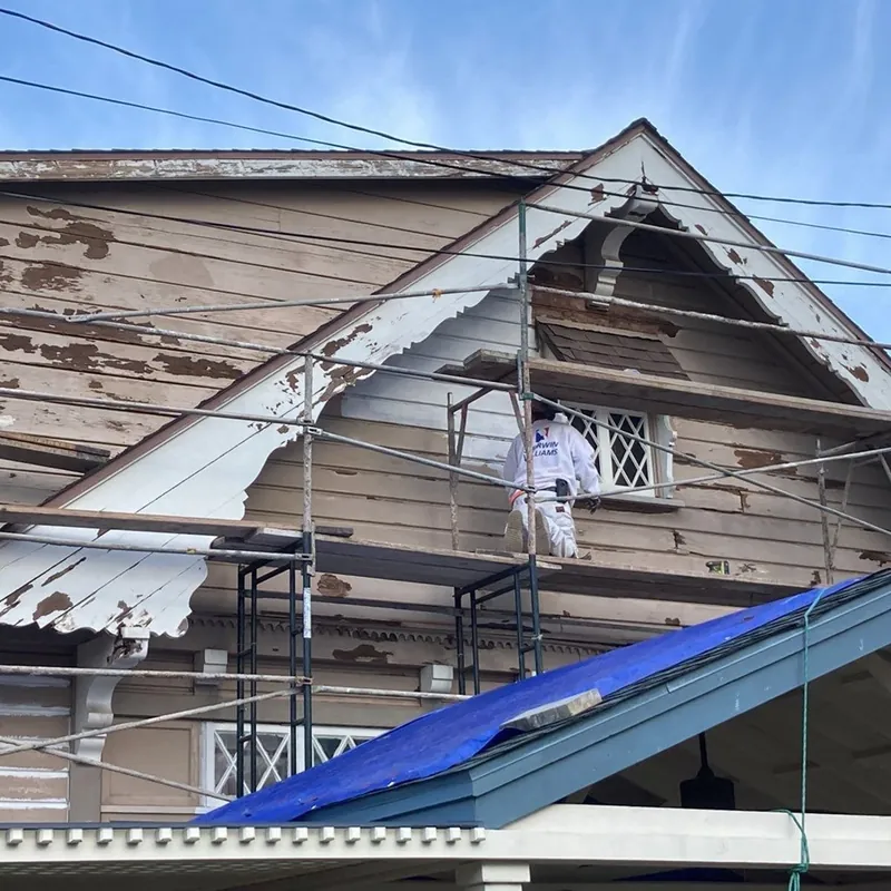 Painter on scaffolding stripping failed paint from a historic gable
